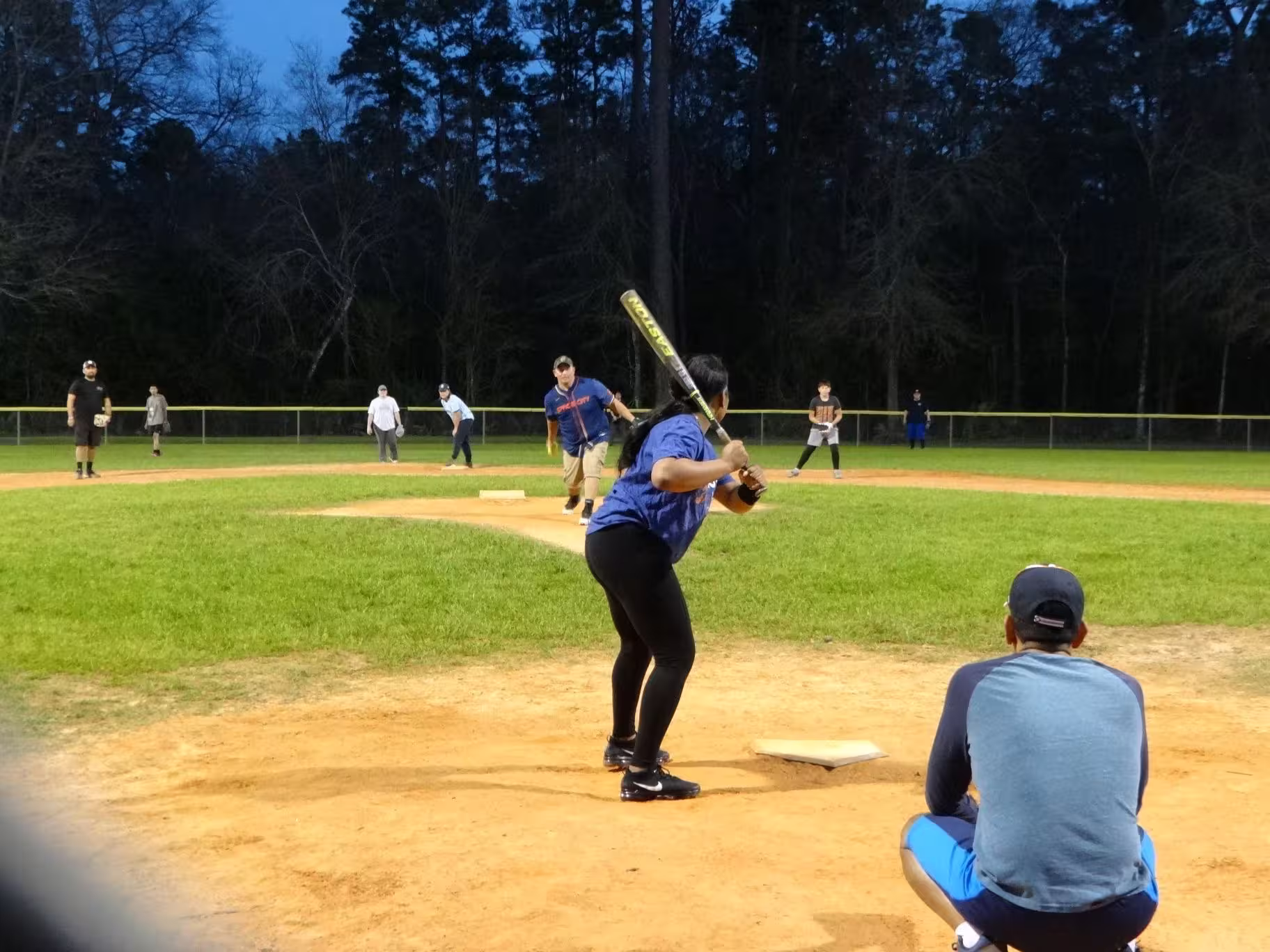 One of the members by homeplate ready to bat. Nice view of the field, pitcher, and several other players.